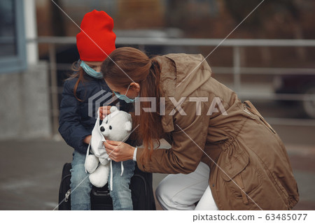 A European mother in a respirator with her daughter are standing near a building.The parent is teaching her child how to wear protective mask to save herself from virus 63485077