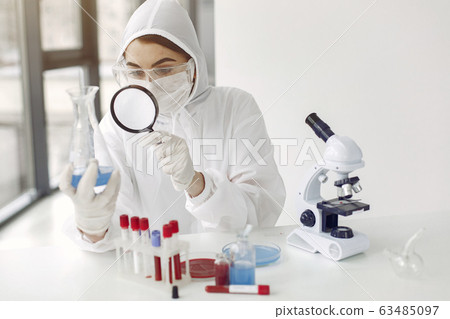 A laboratory scientist is examining blue solution in a bottle 63485097