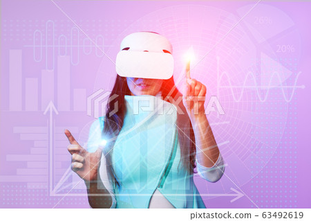Woman uses a virtual reality headset to work with data in the form of graphs and charts. 63492619