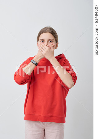 Pretty teenager in red hoodie and white jeans covering her mouth by hands 63494607