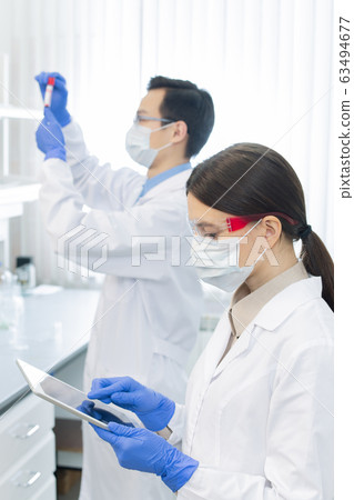 Female lab worker in protective mask, eyewear, gloves and whitecoat using tablet Female lab worker in protective mask, eyewear, gloves and whitecoat using tablet 63494677