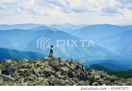 Rear view girl is opening her arms standing on top of cliff with powerful view mountain valley 63497971