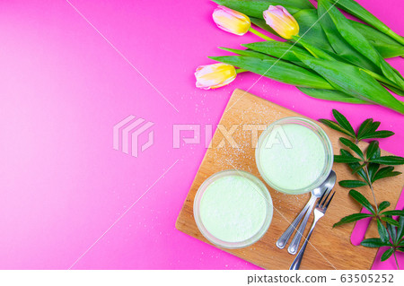 Mint lemon yogurt with kiwi in salad bowls on a wooden board along with tulips on a pink background 63505252
