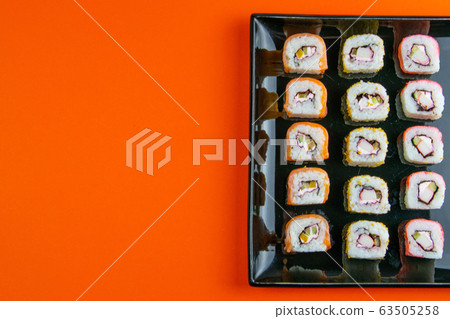 Black plate with sushi, filled with rolls of different kinds, next to stand sticks for sushi, red marinaginger and soy sauce. Black plate with sushi, filled with rolls of different kinds, next to stand sticks for sushi, red marinaginger and soy sauce. 63505258