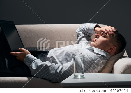 businessman is lying on the sofa with laptop and 63507434