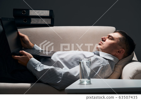 businessman is lying on the sofa with laptop and 63507435