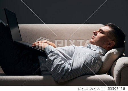 businessman is lying on the sofa and working with 63507436