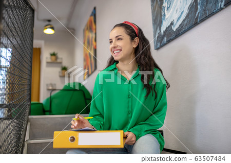 Young woman sitting on stairs with yellow folder on her lap. 63507484