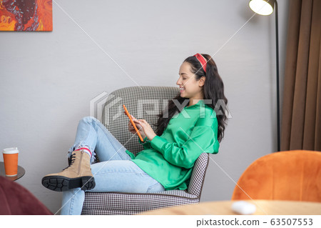 One woman looking into a tablet computer sitting in an armchair. 63507553