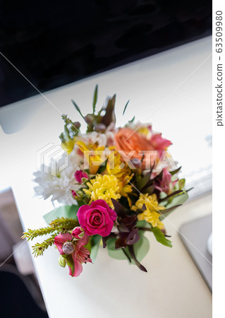 A stylish bouquet with fresh spring flowers is on the desktop near the computer, keyboard and mouse 63509980