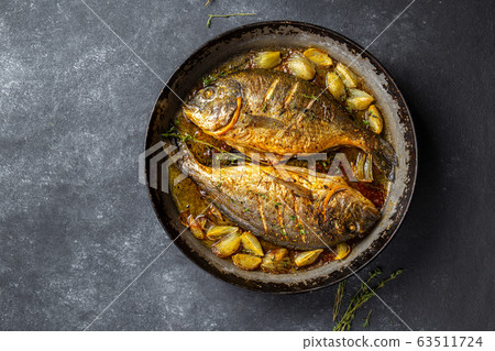 Baked sea bream or dorada with onion and herbs in pan on dark background Baked sea bream or dorada with onion and herbs in pan on dark background 63511724
