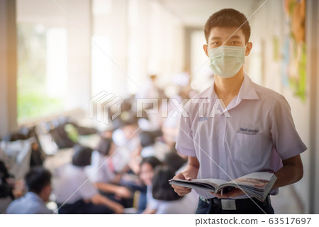 The Asian high school students in the white school uniforms wearing the masks to reading the books to prepare final exams in the midst of Coronavirus disease 2019 (COVID-19) epidemic. 63517697