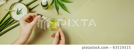 Pipette with CBD cosmetic oil in female hands on a green background with cosmetics, cream with cannabis and hemp leaves, marijuana Banner 63519315