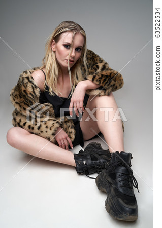 Young blonde woman in leopard coat and boots looking at camera while sitting in studio 63522534
