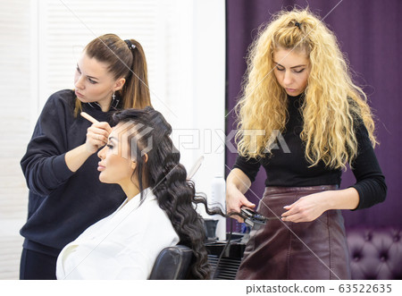 Makeup artist and hairdresser work with beautiful young girl in beauty salon 63522635