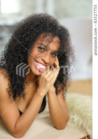 Young afro american female person lying leaning on elbows and wearing bra. 63527755