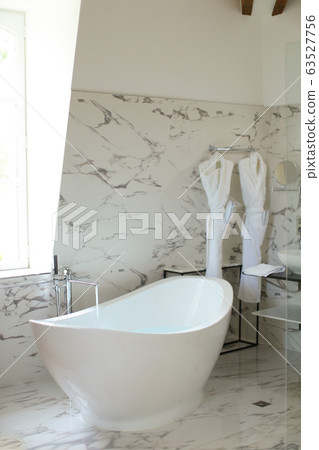 Modern light marble bathroom and ceramic bath near window. 63527756