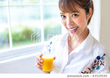 Woman drinking orange juice by the window Woman drinking orange juice by the window 63529595