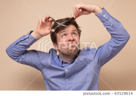 Handsome shaggy man with scissors trying to cut Handsome shaggy man with scissors trying to cut 63529614