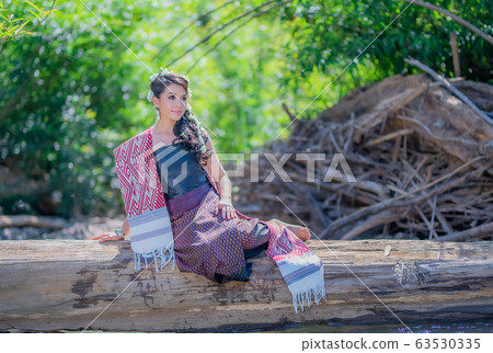 Beautiful Thai women wearing traditional Thai clothes sitting on a log in the river. Woman concept. Beautiful Thai women wearing traditional Thai clothes sitting on a log in the river. Woman concept. 63530335