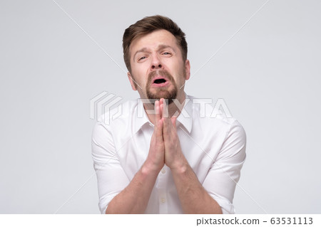 Emotive guy clenching hands together frowning Emotive guy clenching hands together frowning 63531113