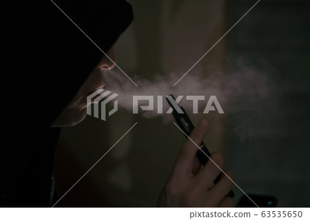 Vaper / A man smoking an electronic cigarette in a dark room Vaper / A man smoking an electronic cigarette in a dark room 63535650