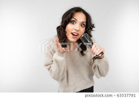 brunette girl in a white sweater holds a retro microphone in her hand and sings a song on a white 63537791