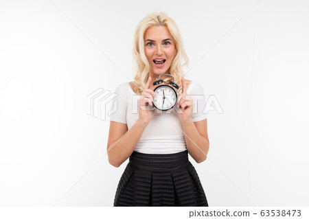 blond girl in a white t-shirt holds an alarm clock on a white background with copy space 63538473