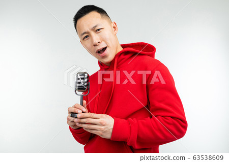 brunette guy in a red sweater sings into a retro microphone on a white background brunette guy in a red sweater sings into a retro microphone on a white background 63538609