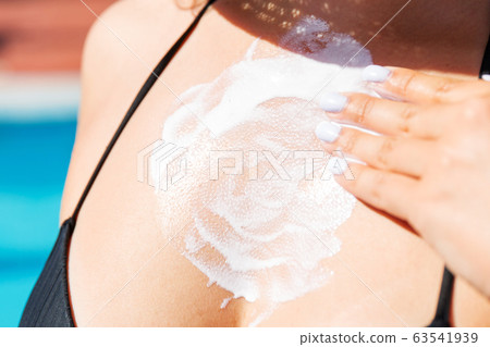 Pretty girl putting sun cream on her breast near 63541939