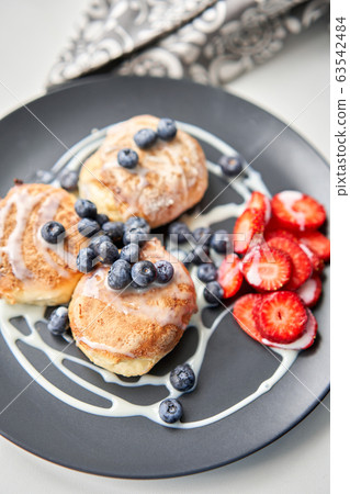 Cottage cheese pancakes or syrniki with blueberry and strawberries on black plate, closeup view. Condensed milk sauce. Russian, Ukrainian cuisine. Healthy tasty breakfast Cottage cheese pancakes or syrniki with blueberry and strawberries on black plate, closeup view. Condensed milk sauce. Russian, Ukrainian cuisine. Healthy tasty breakfast 63542484