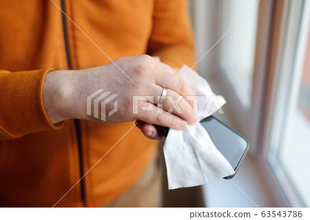 Mature man wipes with a disinfecting cloth his smartphone Mature man wipes with a disinfecting cloth his smartphone 63543786