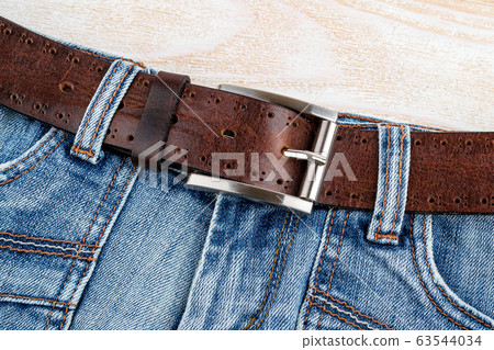 Jeans with brown genuine leather belt with classic metal buckle on a wooden background. Jeans with brown genuine leather belt with classic metal buckle on a wooden background. 63544034