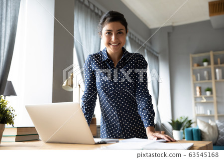 Portrait smiling Indian girl standing at desk with laptop Portrait smiling Indian girl standing at desk with laptop 63545168