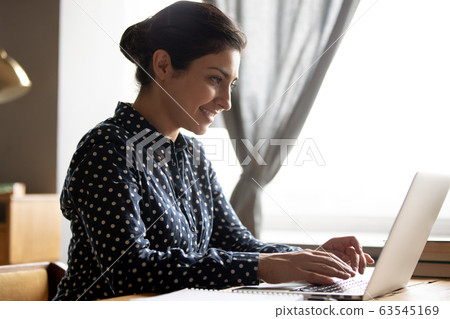 Smiling Indian woman working on laptop, typing on keyboard Smiling Indian woman working on laptop, typing on keyboard 63545169