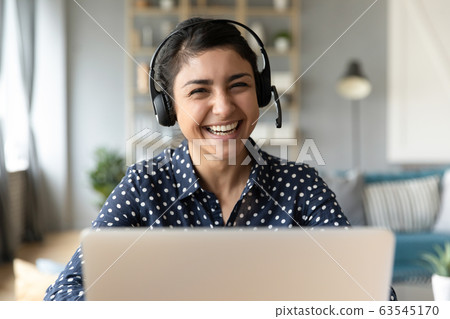 Head shot portrait smiling Indian woman wearing headphones at workplace Head shot portrait smiling Indian woman wearing headphones at workplace 63545170