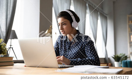 Busy young Indian woman wearing headphones working on laptop Busy young Indian woman wearing headphones working on laptop 63545172