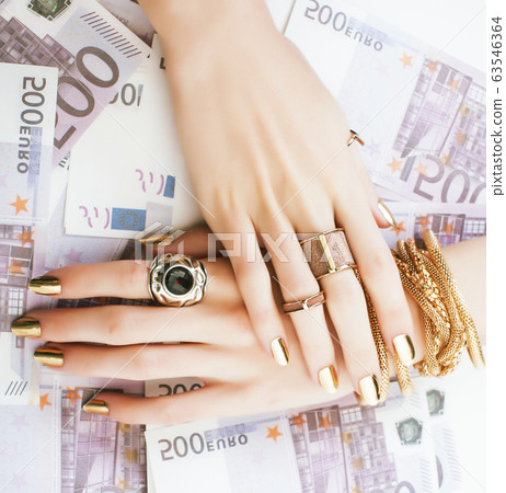 hands of rich woman with golden manicure and many jewelry rings on cash euros 63546364