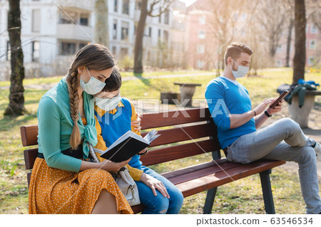 People sitting on park bench in the sun practicing social distancing 63546534