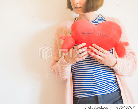 Young woman hugging red heart shaped plush toy 63546767