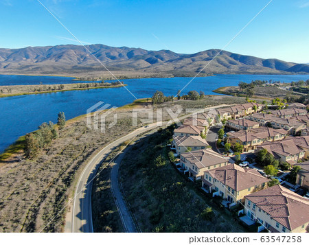 Aerial view of identical residential subdivision house with big lake and mountain on the background during sunny day  63547258