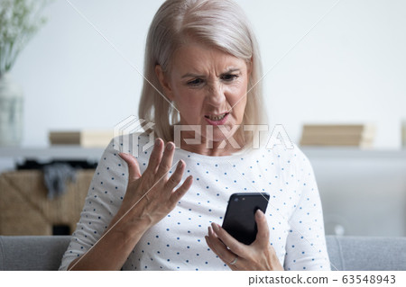 Unhappy middle aged lady irritated by bad smartphone work. 63548943