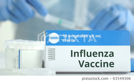 Box with influenza vaccine on the table against blurred lab assistant or doctor. Fictional phaceutical logo Box with influenza vaccine on the table against blurred lab assistant or doctor. Fictional phaceutical logo 63549306