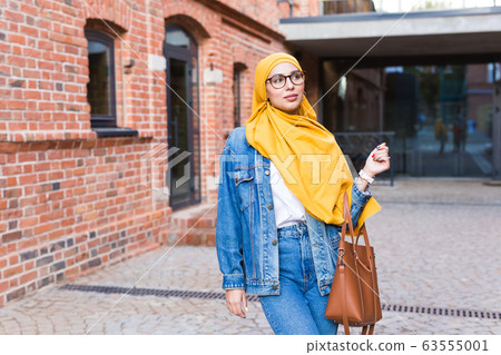 Beautiful Arabic muslim woman wearing yellow hijab, stylish female portrait over city street. 63555001