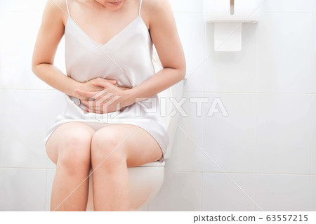 Women wearing white sleepwear, Sitting on the toilet Hand holding the stomach,standing in the toilet, Holding a toilet paper, bent, stomachache health care concept 63557215