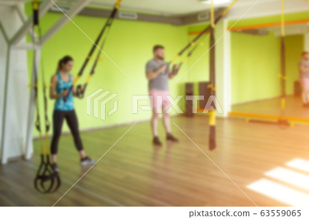 The trainer teaches in the gym to practice a man on the hinges of the TRX while performing an exercise facial thrust, blurred The trainer teaches in the gym to practice a man on the hinges of the TRX while performing an exercise facial thrust, blurred 63559065