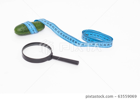 Cucumber with a measuring tape and a magnifying glass on a white background. Genital size concept in a man, penis enlargement Cucumber with a measuring tape and a magnifying glass on a white background. Genital size concept in a man, penis enlargement 63559069