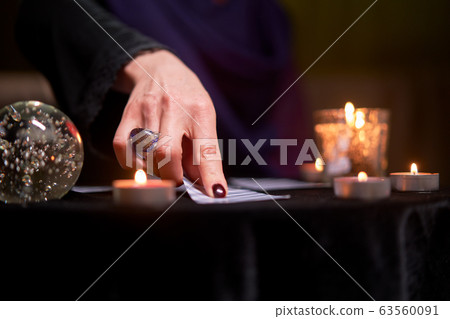 Close-up of fortune teller woman divining on cards sitting at table with burning candles, magic ball 63560091