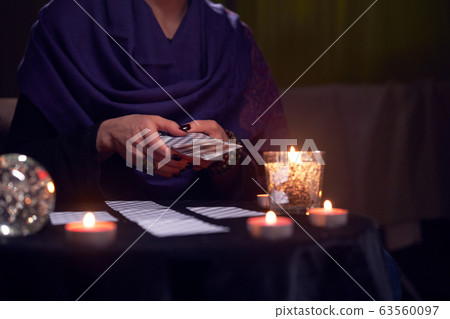 Close-up of soothsayer female guessing on cards sitting at table with burning candles, magic ball 63560097