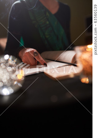 Close-up of female fortune-teller's hands, book of predictions, burning candle Close-up of female fortune-teller's hands, book of predictions, burning candle 63560139